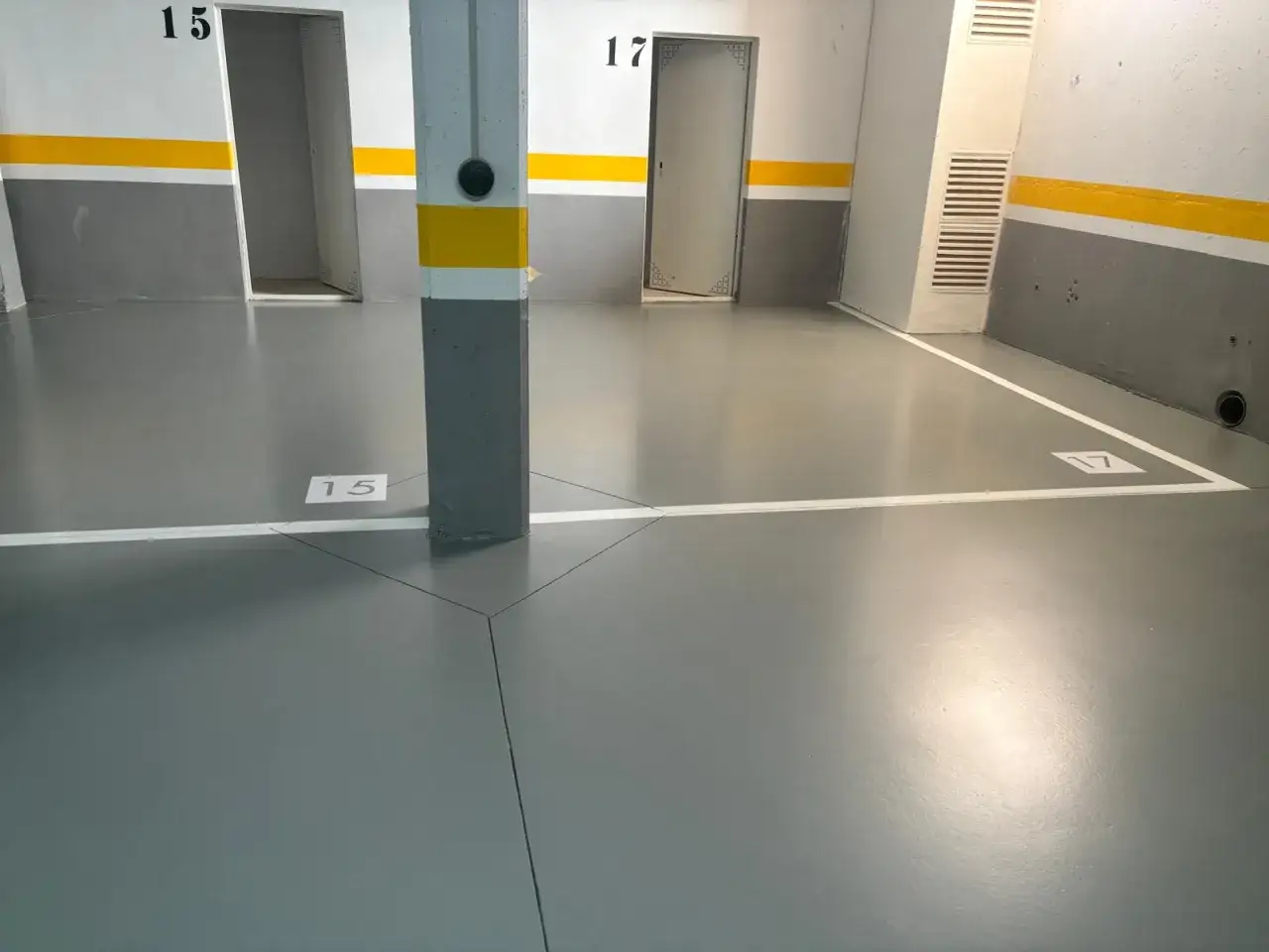 Suelo de garaje con pintura epoxi gris, señalizado con líneas blancas y números de plaza.