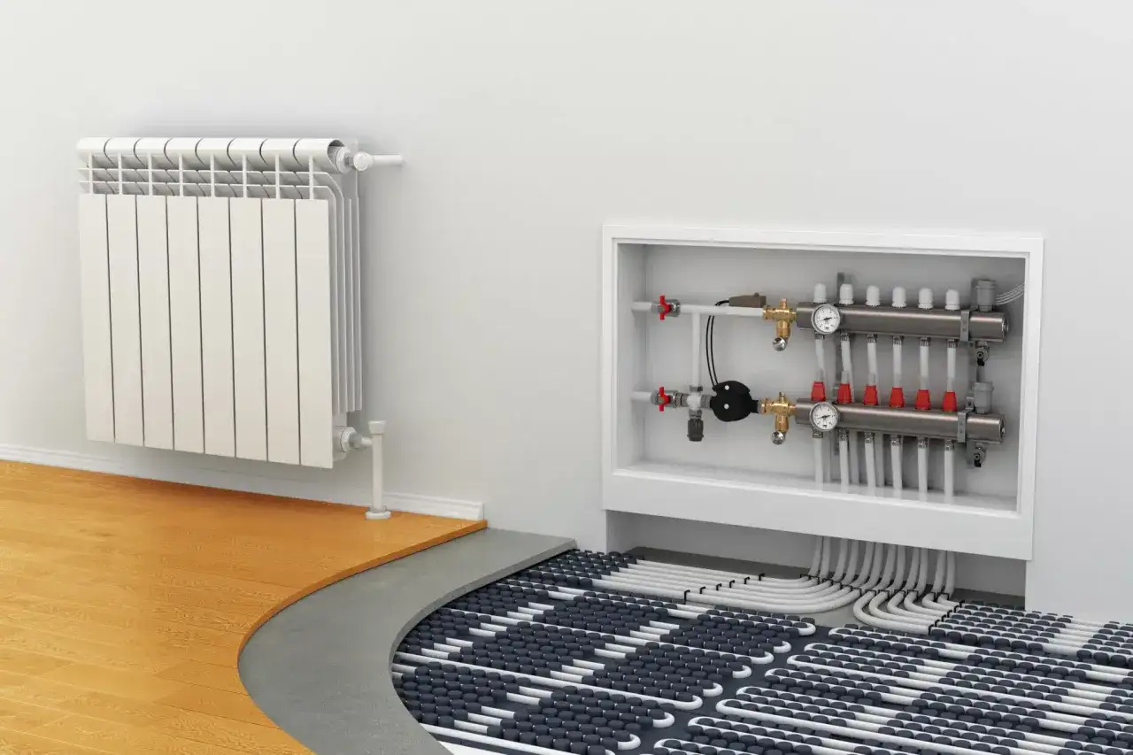 Instalaci&oacute;n de radiadores y suelo radiante. Un radiador blanco est&aacute; en la pared, junto a un colector de calefacci&oacute;n y tuber&iacute;as de suelo radiante.