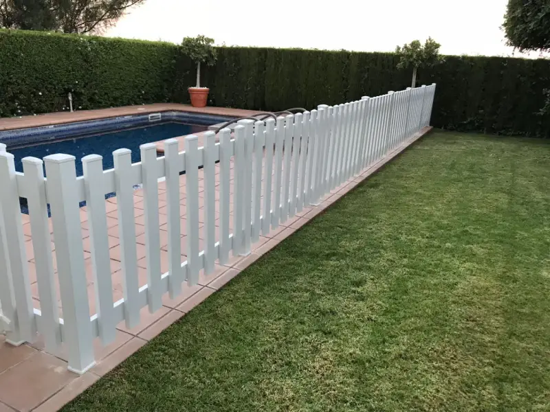 Una verja de jardín blanca protege una piscina y un césped verde.