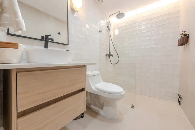 Baño moderno con lavabo sobre mueble de madera, inodoro y ducha con azulejos blancos. ¡Un proyecto de pintar azulejos baño que inspira!