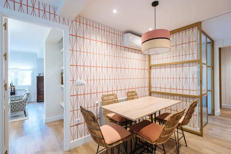 Comedor con pared empapelada con un diseño geométrico en naranja. Mesa de madera con sillas de ratán y cojines terracota.